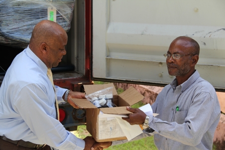 (L-R) Minister of Health in the Nevis Island Administration hands over a box of wound dressing supplies as he hands over the 40 feet container with medical supplies, equipment and furnishings (in the background) to Hospital Administrator Mr. Joe Claxton